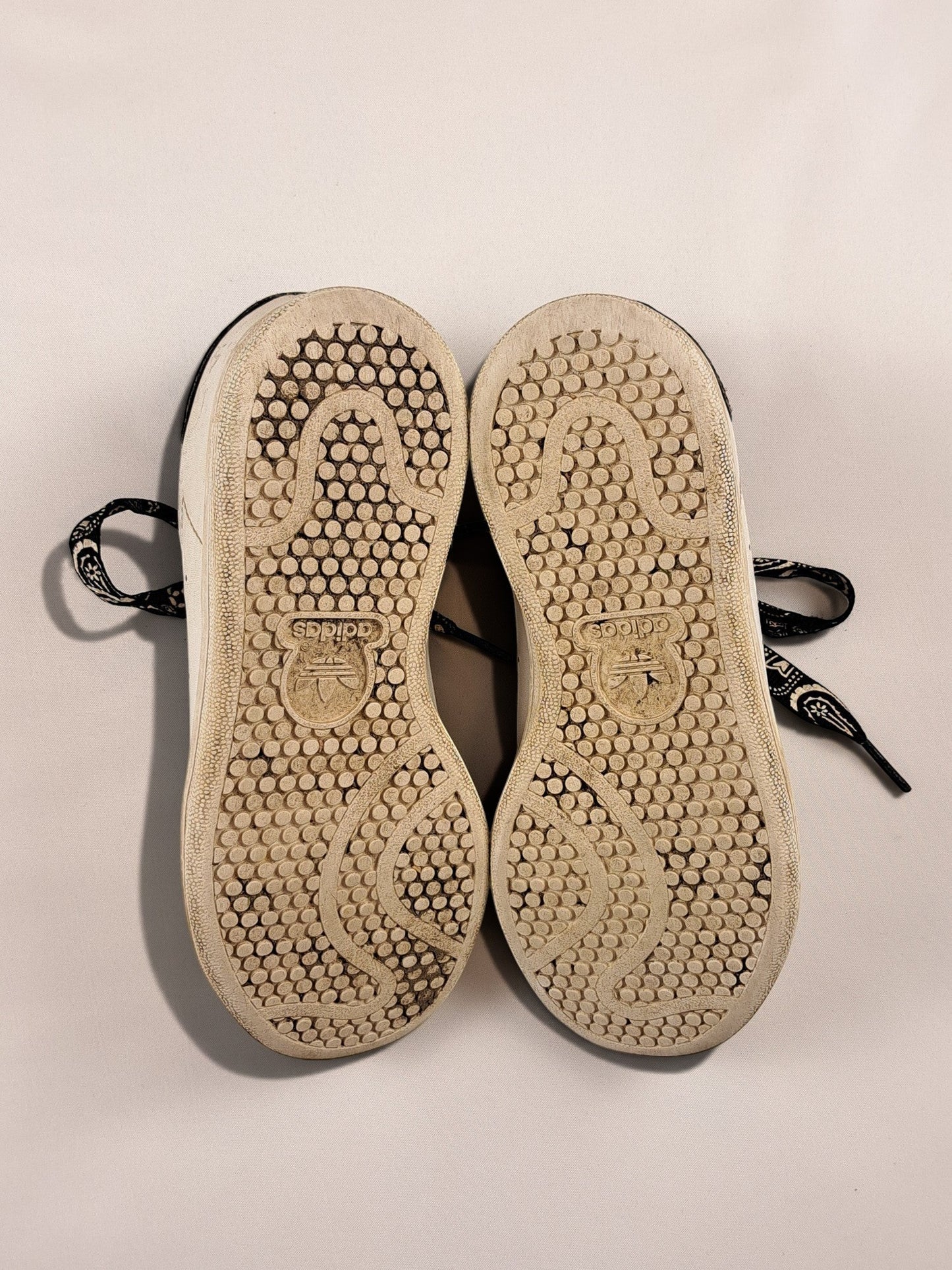 BaraBarnet Adidas sneakers showing the worn rubber outsoles with a circular tread pattern and black paisley laces.