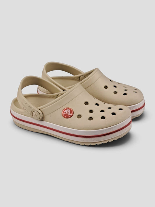 BaraBarnet beige Crocs rubber clogs with perforated holes, heel straps, and red stripe detail for kids.