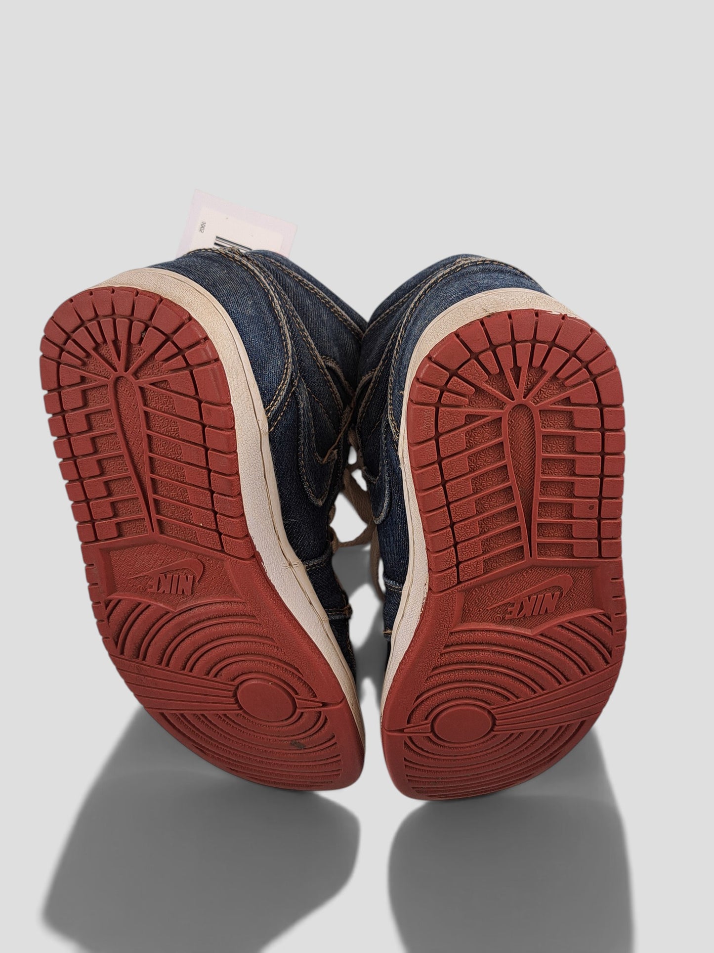 BaraBarnet Levi's x Nike denim high-top sneakers with red rubber outsoles, viewed from the bottom.