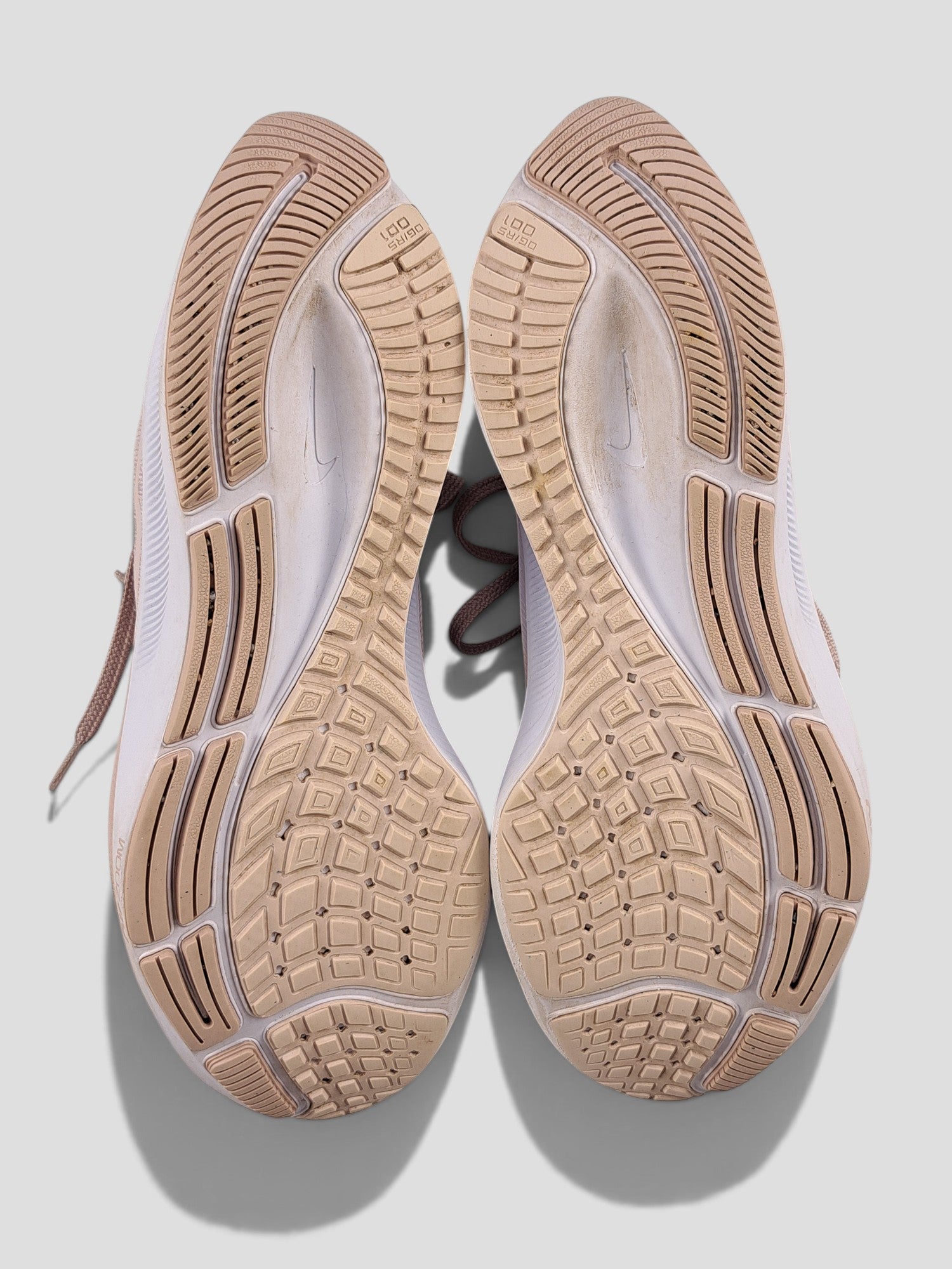BaraBarnet Nike running shoes with beige rubber outsoles and white midsoles, bottom view showing tread pattern.